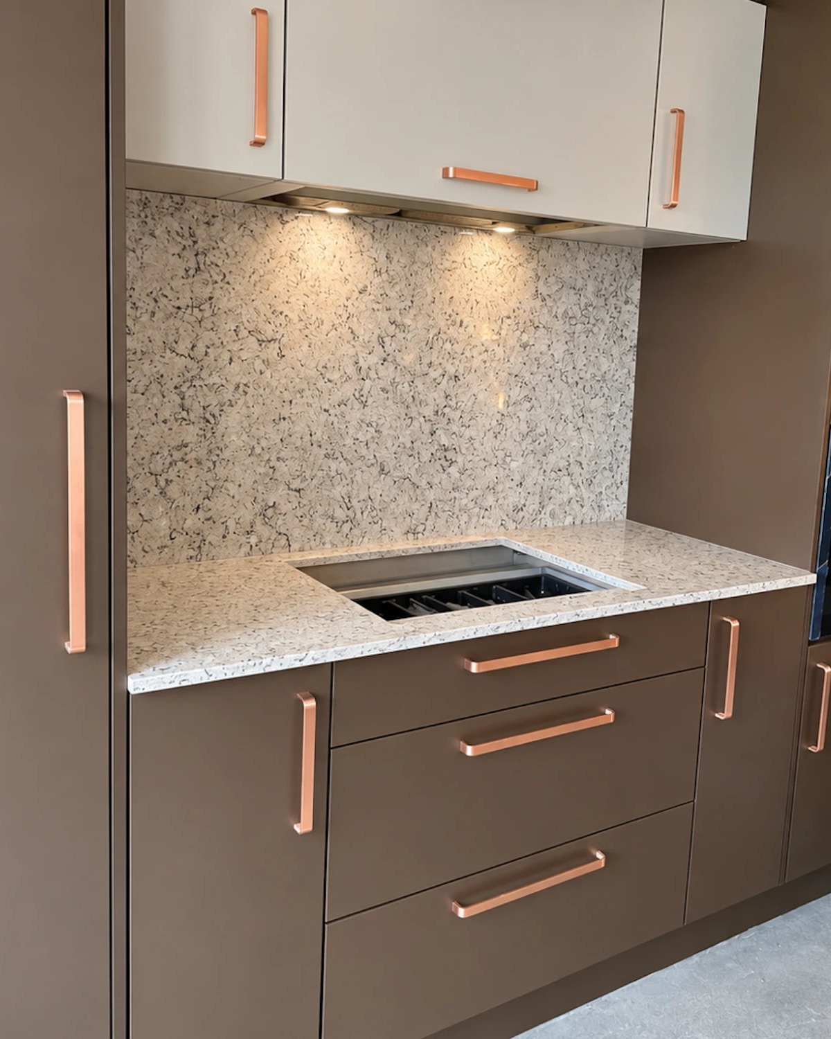 Completed kitchen detail: bronze cabinetry with copper handles, stone-effect worktop and full-height splashback